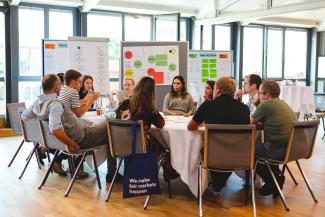 group of people sitting at a table, a board in the back